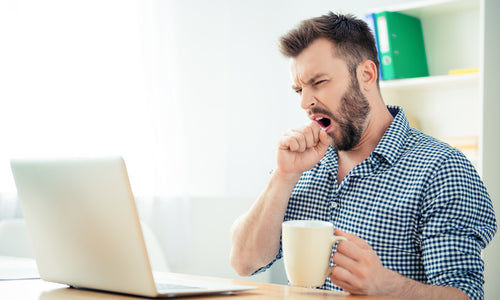 man yawning in front of laptop